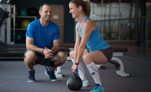 trainer watching a member using a weighted ball to do squat lifts
