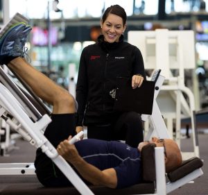 photo of woman watching over man doing leg presses