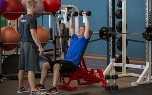 trainer watching over a man doing weight lifting with small free weights
