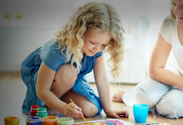 photo of woman watching over a child coloring using paints